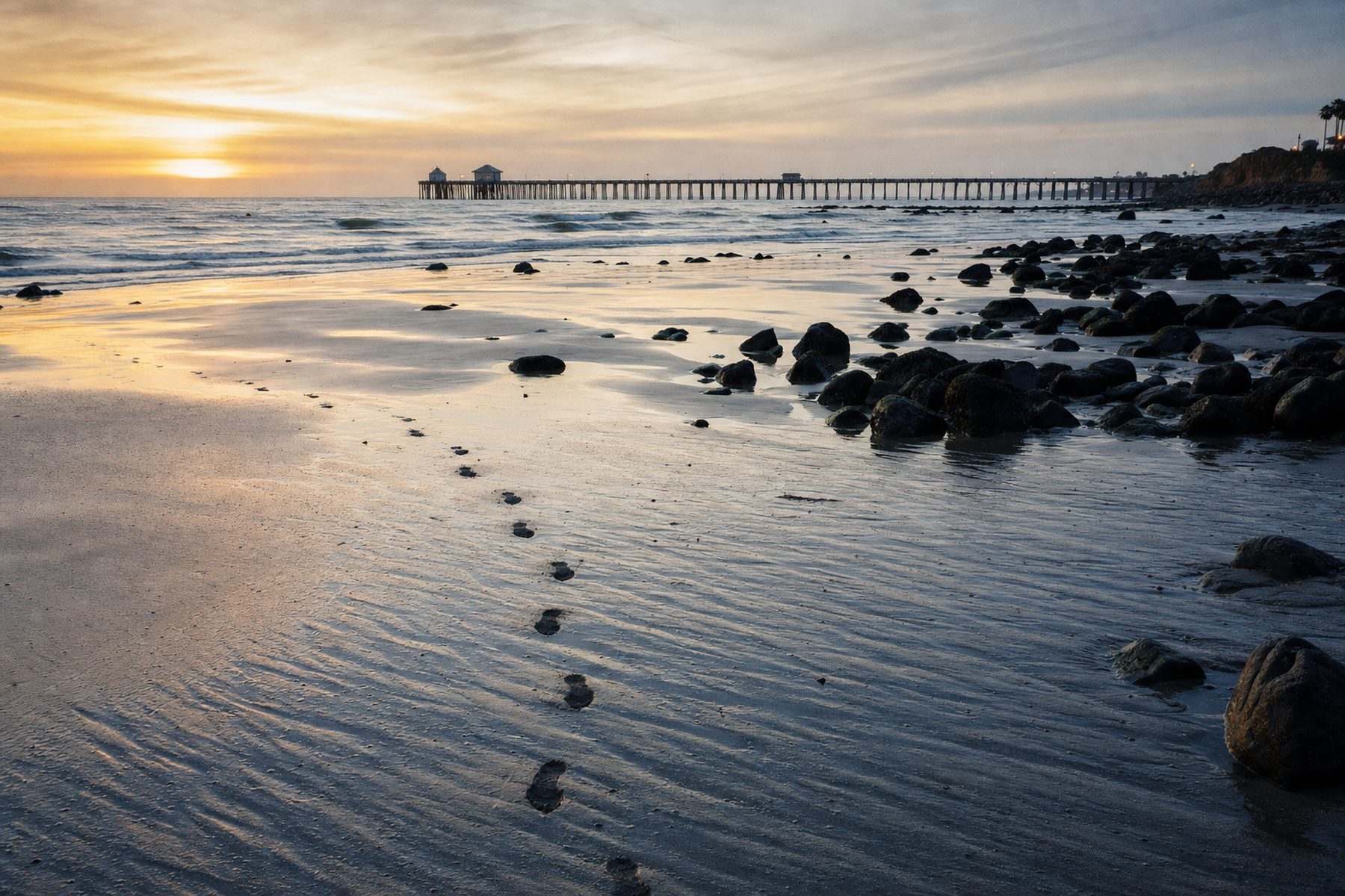 A Southern California beach at dawn during an extreme low tide, wet rippled sand and a distant pier